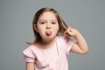Funny little girl showing her tongue on grey background © New Africa