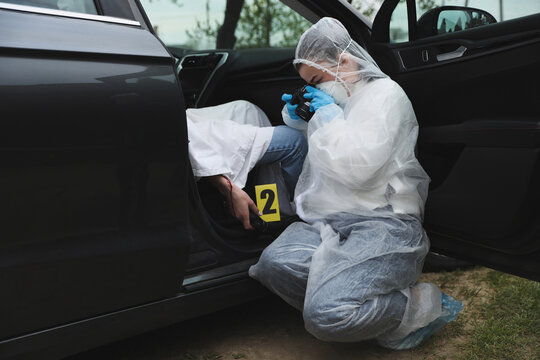 Criminologist taking photo of evidence at crime scene with dead body in car