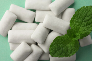 Tasty white chewing gums and mint leaves on turquoise background, top view