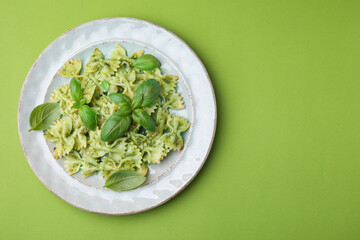 Delicious pasta with pesto sauce and basil on light green background, top view. Space for text
