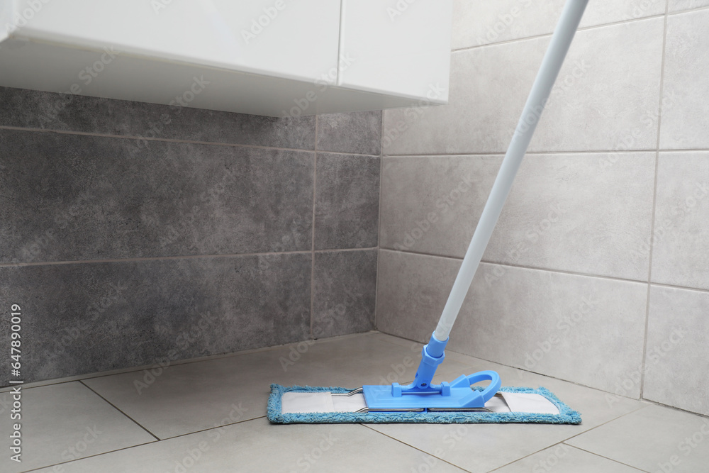 Poster Cleaning grey tiled floor with mop indoors