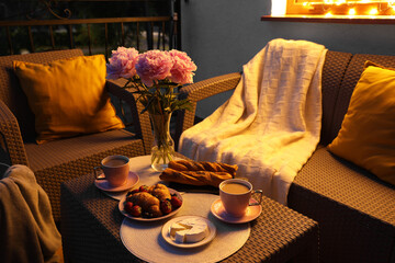 Rattan table with drink, food and flowers on outdoor terrace in evening
