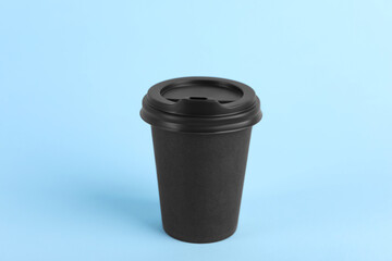 Black paper cup with plastic lid on light blue background. Coffee to go