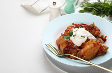 Delicious stuffed cabbage rolls served with sour cream on white table, closeup. Space for text