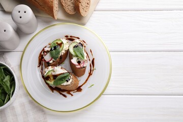 Delicious bruschettas with cream cheese, vegetables, balsamic vinegar and ingredients on white wooden table, flat lay. Space for text