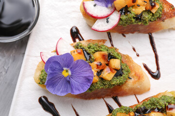 Delicious bruschettas with pesto sauce, tomatoes, balsamic vinegar and violet flower on table, above view