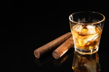 Glass of whiskey with ice cubes and cigars on black mirror surface. Space for text