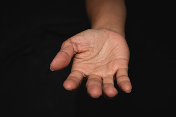 Open hands of wrinkled middle-aged woman praying for God's blessing on black background.