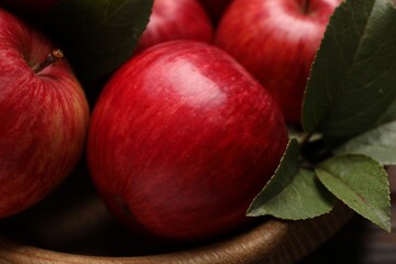 Ripe red apples and green leaves in wooden bowl on table, closeup