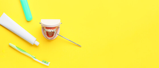 Model of jaw with dental braces, dentist's tool, tooth brush and paste on yellow background with...