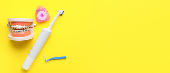 Model of jaw with dental braces, tooth brushes and floss on yellow background with space for text