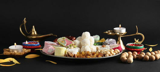 Plate with Indian treats and lamps on dark background. Divaly celebration