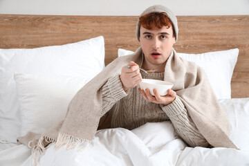 Ill young man eating soup in bedroom