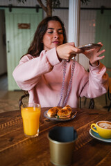Young woman taking a photo of her brunch to share it on social media. Bagel sandwich and coffee.