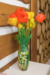 Red and yellow flowers tulips stand in a vase in a wooden interior