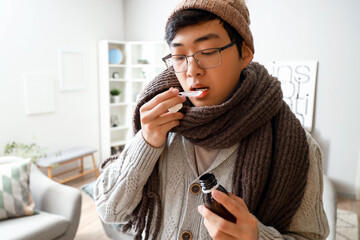 Ill Asian man with cough syrup at home, closeup