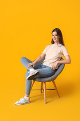 Fototapeta na wymiar Young woman sitting in armchair on yellow background