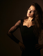 Fototapeta premium Beautiful makeup sexy elegant woman standing with healthy long hair in style fashion black dress on black shadow dark background with empty copy space. Closeup front portrait.