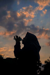 Silhouette of a woman wearing a hijab drinking bottled water with a sunset background 