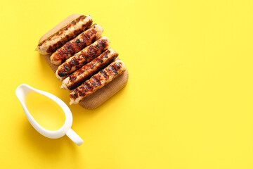 Wooden board of tasty grilled sausages and oil on yellow background