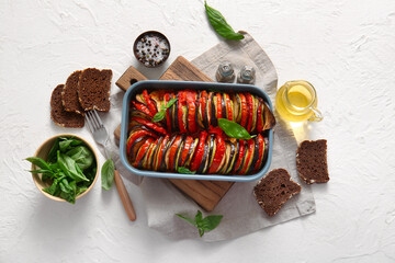 Baking dish of tasty Ratatouille, bread, oil and spices on white background