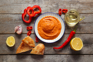 Plate of tasty muhammara and ingredients on wooden background