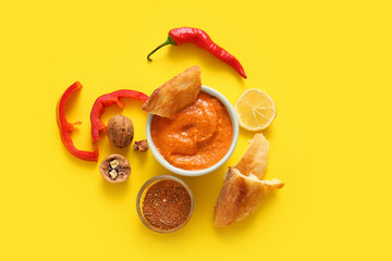 Bowl of tasty muhammara and ingredients on yellow background