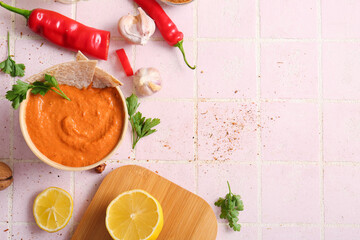 Bowl of tasty muhammara and ingredients on pink tile background