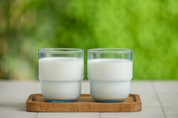 Wooden board with glasses of fresh milk on white tile table outdoors