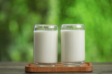 Board with glasses of fresh milk on wooden table outdoors
