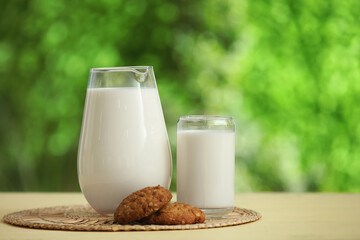 Glass and jug of fresh milk with sweet cookies on yellow wooden table outdoors