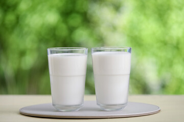 Glasses of fresh milk on yellow wooden table outdoors