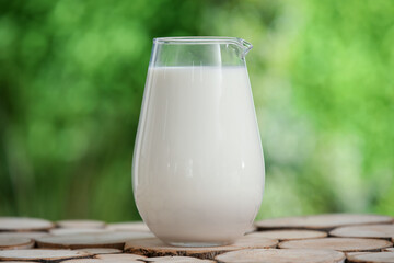 Jug of fresh milk on wooden table outdoors