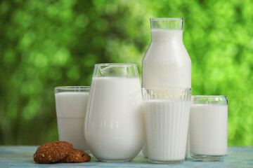 Glasses and jug of fresh milk with sweet cookies on blue table outdoors