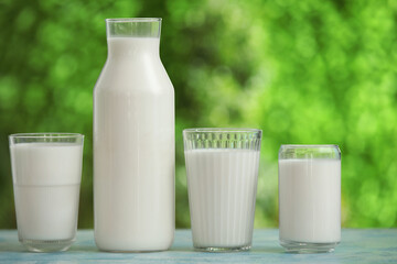 Glasses and bottle of fresh milk on blue table outdoors