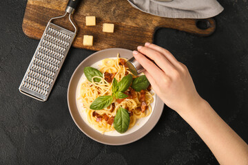 Woman adding spices onto plate with tasty pasta carbonara on black background