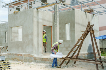 Asian architect and engineer inspecting the structure of a house under construction. Wear green...