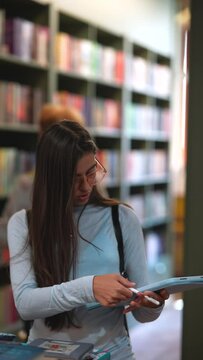 Surrounded by books, a stunning young woman is leisurely wandering through the bookstore.