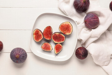 Plate with cut fresh figs on white wooden background