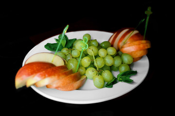 Fruity white plate with fresh green grapes and sliced apple slices on a black background