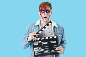 Shocked young man dressed for Halloween as zombie with movie clapper on blue background