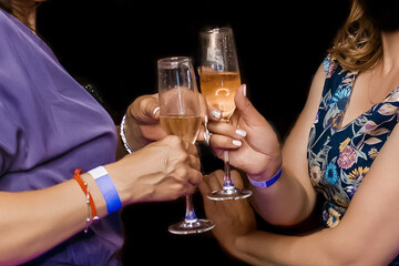 Two adult women clinking glasses of chilled champagne alcohol on a dark background, close-up