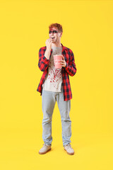 Young man dressed for Halloween eating popcorn on yellow background