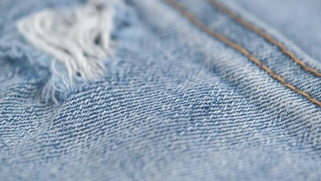 closeup rotation of blue ripped jeans with a hole. torn texture of the fabric. hole in jeans. seams are stitched with yellow threads. concept of sewing and repairing clothes.