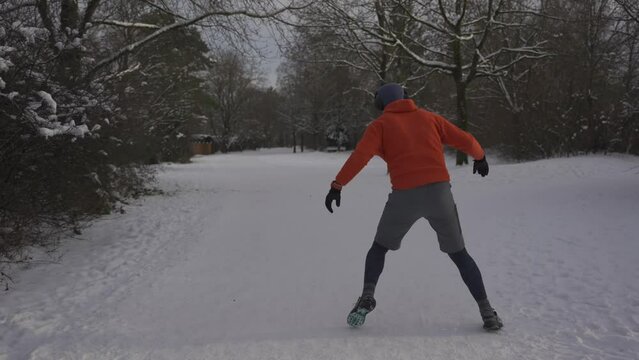 Wrong outfit and footwear for running on slippery surfaces in winter. Man jogging in snow cold weather and slips. Slippery sneakers with wrong soles for trail running on ice covered paths in woods. 