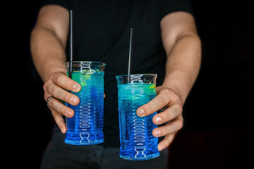 Bartender's hands serve 2 alcoholic cocktails with blue syrup blue lagoon in the black background