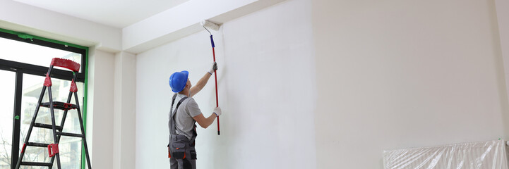 Male painter paints house wall with roller brush.