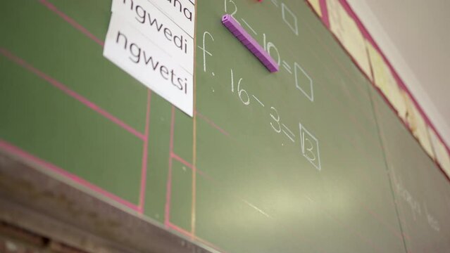School chalkboard in South African classroom with math sums and African language words.