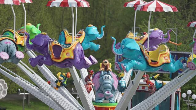 A marry-go-round with elephant-shaped seats in the amusement park. Slow-motion, parallax shot.