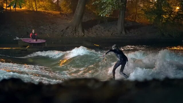 Cinematic fade inslow motion Eisbach Wave River Surfer community Munich Germany ground level fall autumn beautiful night surfing high flow water surf Upper Bavaria Alps flow follow movement
